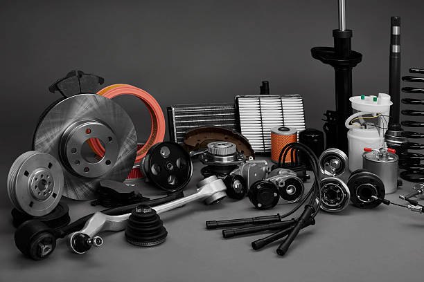 Genuine vehicle spares laid out — brake disc, filters, shock absorber, suspension arm and belts